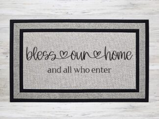 Mockup of a doormat that says, "Bless our home, and all who enter" in a cute cursive flourish font.