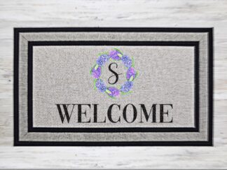 Mockup of a custom welcome mat with monogram in a purple floral wreath, with the word welcome underneath