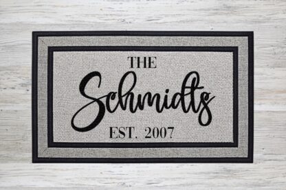 Mockup of a personalized doormat that features your family's last name in a bold modern script with the year the family was established underneath.