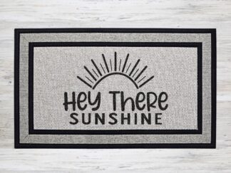 Mockup of a doormat that says, "hey there sunshine" in a bold black font with a sun with lots of rays underneath the text.