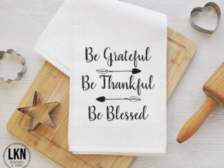 White dish towel with black text 'Be grateful. Be thankful. Be blessed.'