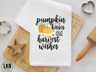 White dish towel with black text 'Pumpkin kisses and harvest wishes'.