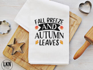 White dish towel with black text 'Fall Breeze and Autumn Leaves'.