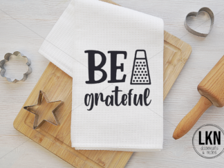White dish towel with black text 'Be grateful'.