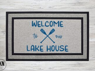 Mockup of a lake themed doormat featuring the phrase, Welcome to out Lake House, with a pair of oars in the center.