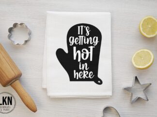 White dish towel with white text 'It's getting hot in here' paired with black oven mitt.