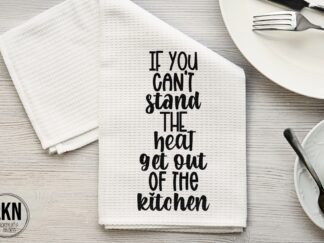 White dish towel with black text: "If you can't stand the heat, get out of the kitchen." Motivational kitchen quote on a practical towel.
