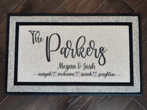 Doormat: Large handwriting font displaying last name. Below: Couple's first names & children's names. A personalized welcome for the whole family.