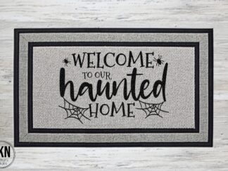 Mockup of a Halloween themed doormat that says "welcome to our haunted home" in a bold black font with some spiderwebs and spiders.