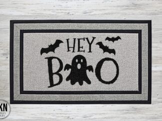 Mockup of a Halloween themed doormat that says "hey boo" in a bold black font with a cute ghost.