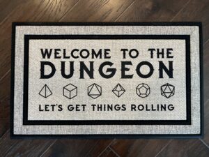 Picture of a doormat that says "Welcome to the Dungeon" with various sized die under it, and then the phrase "Let's get things rolling"