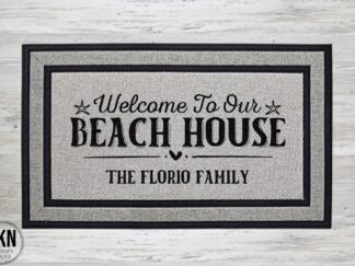 Mockup of a beach themed doormat that says "Welcome to Our Beach House" in a bold black font and is personalized with the family last name underneath.