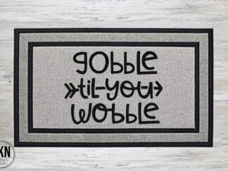 Mockup of a Thanksgiving themed doormat that says "Gobble til you Wobble" in a bold black font
