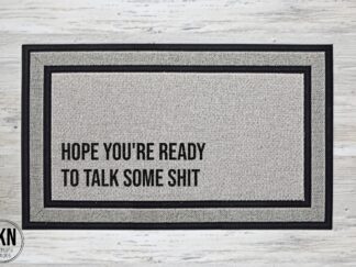 Mockup of a sassy welcome mat featuring the phrase, "hope you're ready to talk shit" in a bold font in the bottom left corner of the mat